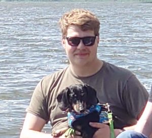 Jared sitting on dock holding dachshund